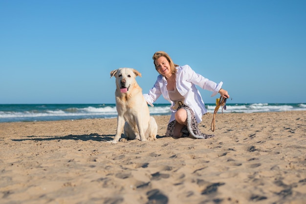 Mulher de meia idade e seu cachorro olham para a câmera na praia