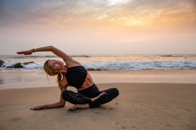 Mulher de meia idade em preto fazendo yoga na praia de areia