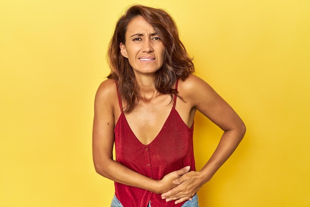 Foto mulher de meia idade em um cenário amarelo com dor de estômago e dor no fígado