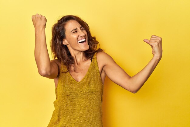 Foto mulher de meia idade em um pano de fundo amarelo levantando o punho após um conceito de vencedor de vitória