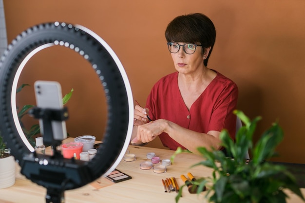 Mulher de meia idade falando sobre cosméticos com sombras de maquiagem e paleta de blush e pincéis enquanto grava seu vídeo mulher madura fazendo vídeo para seu blog sobre cosméticos