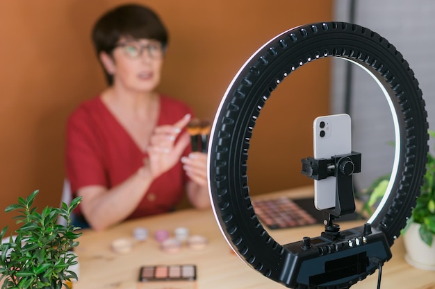 Mulher de meia idade falando sobre cosméticos com sombras de maquiagem e paleta de blush e pincéis enquanto grava seu vídeo mulher madura fazendo vídeo para seu blog sobre cosméticos