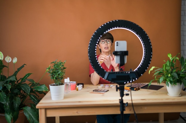 Mulher de meia idade falando sobre cosméticos com sombras de maquiagem e paleta de blush e pincéis enquanto re