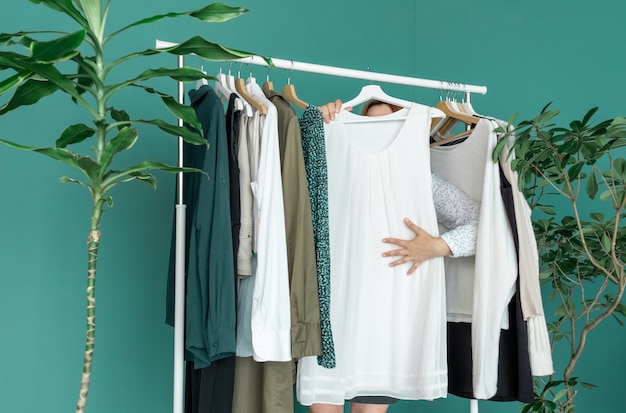 Mulher de meia idade faz compras e olha o vestido novo perto da prateleira com roupas.