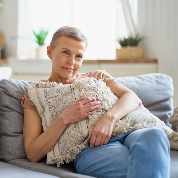 Mulher de meia-idade feliz assistindo TV enquanto está sentada no sofá em casa