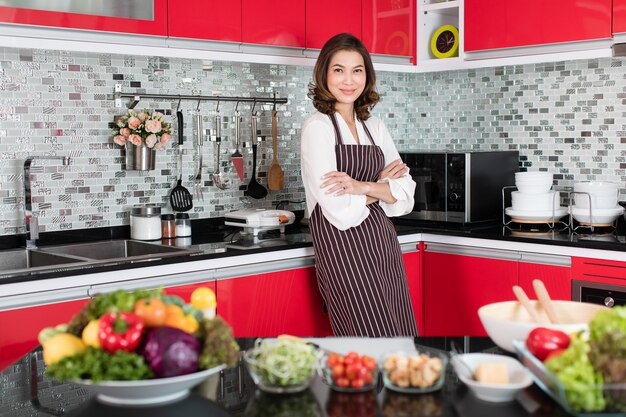 Mulher de meia-idade fofa asiática em um avental de pé e cruzar o braço sobre o peito com gestos de elegância e autoconfiante. conceito de estilo de vida moderno de dona de casa.