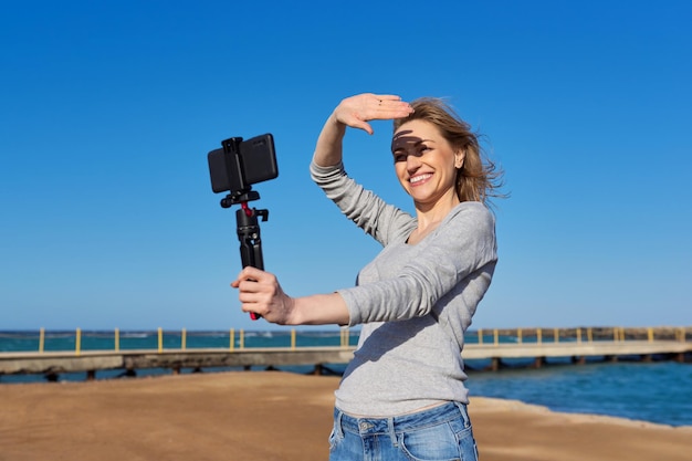 Mulher de meia idade gravando vídeo em smartphone com outdoor na beira-mar