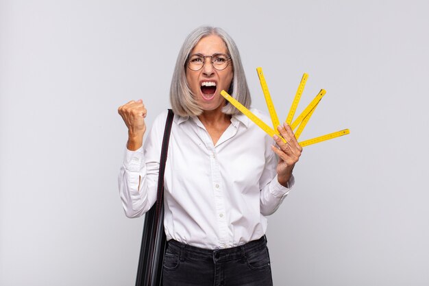 Mulher de meia-idade gritando agressivamente com uma expressão de raiva ou com os punhos cerrados celebrando o sucesso. conceito de arquiteto