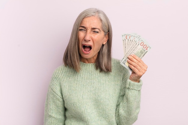 Mulher de meia idade gritando agressivamente olhando o conceito de notas de dólar muito irritado