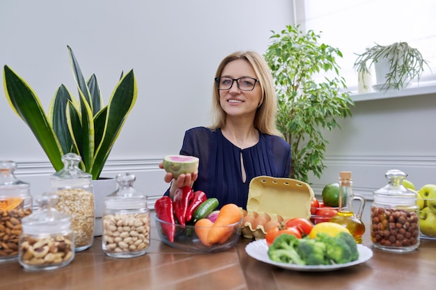 Mulher de meia idade nutricionista profissional sentada à mesa com alimentos melancia rabanete