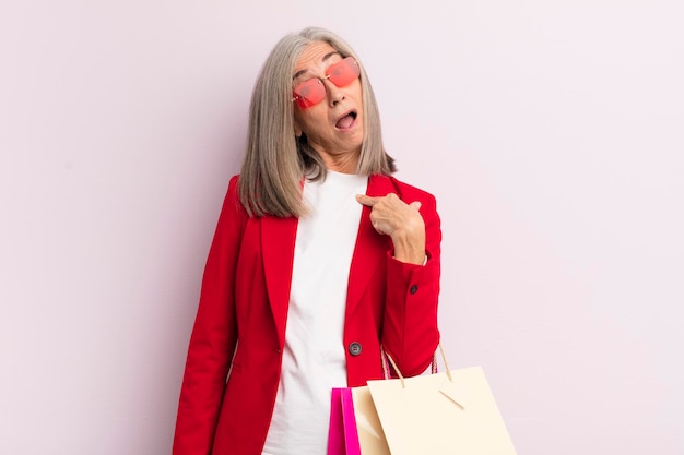 Mulher de meia idade parecendo chocada e surpresa com a boca aberta apontando para o conceito de auto-compras