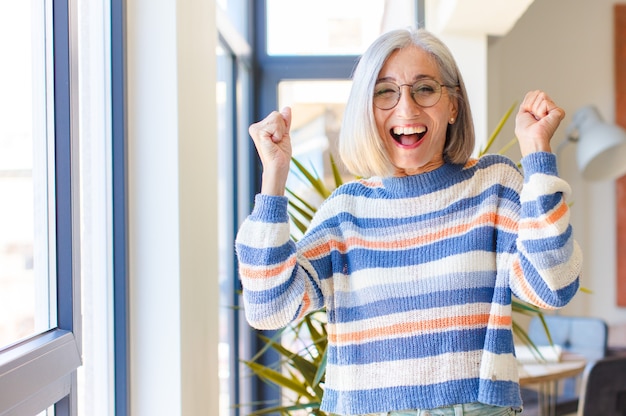 Foto mulher de meia-idade parecendo extremamente feliz e surpresa, comemorando o sucesso, gritando e pulando