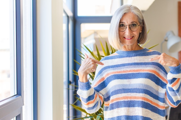 Mulher de meia idade parecendo orgulhosa, positiva e casual apontando para o peito com as duas mãos