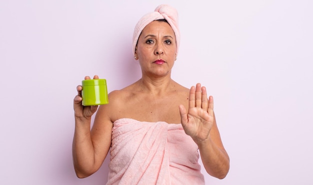 Mulher de meia idade parecendo séria mostrando a palma da mão aberta fazendo gesto de parada chuveiro e conceito de produto de cabelo