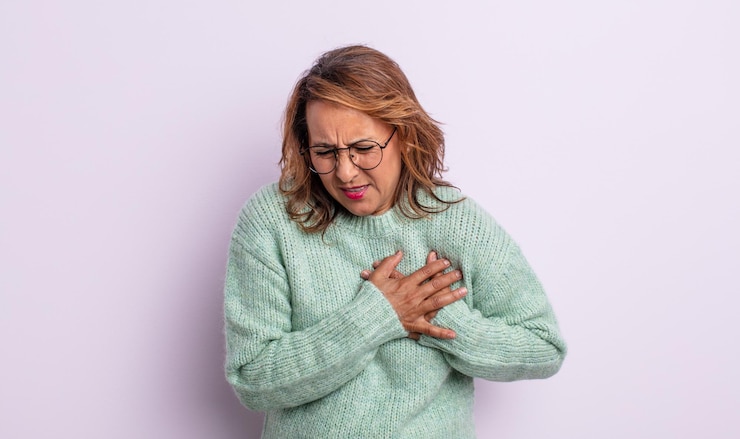 Foto mulher de meia idade parecendo triste, magoada e com o coração partido, segurando as duas mãos perto do coração, chorando e se sentindo deprimida