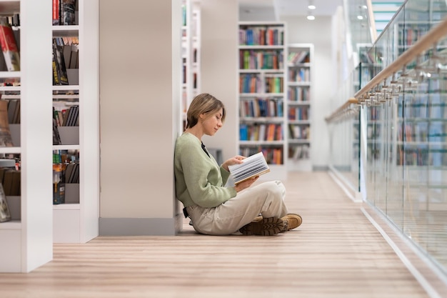 Mulher de meia idade pensativa com livro passando tempo livre na biblioteca gostando de ler