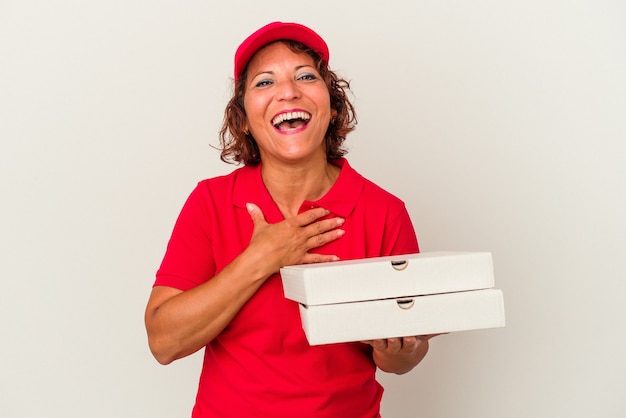 Mulher de meia idade que leva pizzas isoladas no fundo branco ri alto, mantendo a mão no peito.