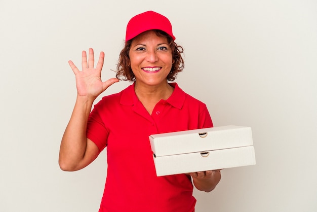 Foto mulher de meia idade que leva pizzas isoladas no fundo branco, sorrindo alegre mostrando o número cinco com os dedos.