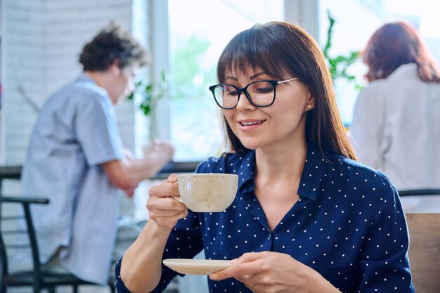 Foto mulher de meia-idade relaxada desfrutando de uma xícara de café perfumado em uma cafeteria