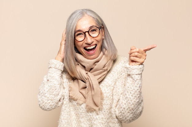 Mulher de meia-idade rindo, parecendo feliz, positiva e surpresa, percebendo uma ótima ideia apontando para o espaço lateral da cópia