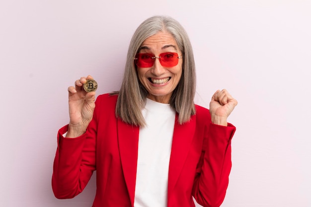 Mulher de meia idade se sentindo chocada rindo e comemorando o conceito de bitcoin de sucesso