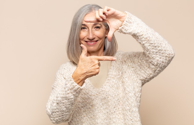 Mulher de meia-idade se sentindo feliz, amigável e positiva, sorrindo e fazendo um retrato ou moldura com as mãos