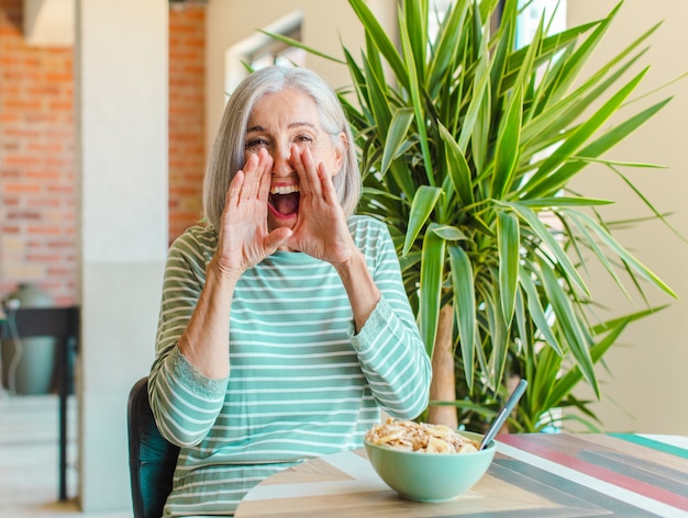 Mulher de meia-idade se sentindo feliz, animada e positiva, dando um grande grito com as mãos perto da boca, gritando