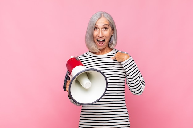 Mulher de meia-idade se sentindo feliz, surpresa e orgulhosa, apontando para si mesma com um olhar animado e surpreso com um megafone