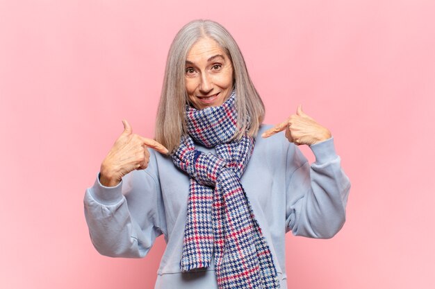 Mulher de meia-idade se sentindo feliz, surpresa e orgulhosa, apontando para si mesma com um olhar animado e surpreso