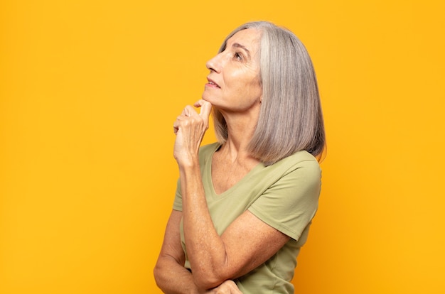 Mulher de meia-idade se sentindo pensativa, imaginando ou imaginando ideias, sonhando acordada e olhando para cima para copiar o espaço