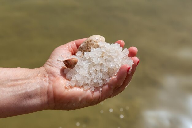 Mulher de meia idade segurando cristais de sal na mão do Mar Morto