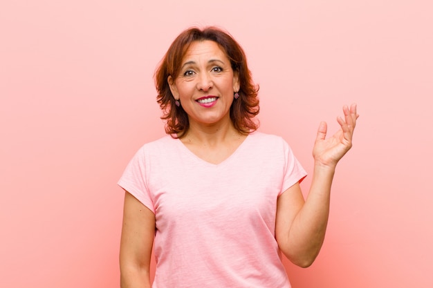 Foto mulher de meia idade, sentindo-se feliz, surpreso e alegre, sorrindo com atitude positiva, percebendo uma solução ou idéia na parede rosa