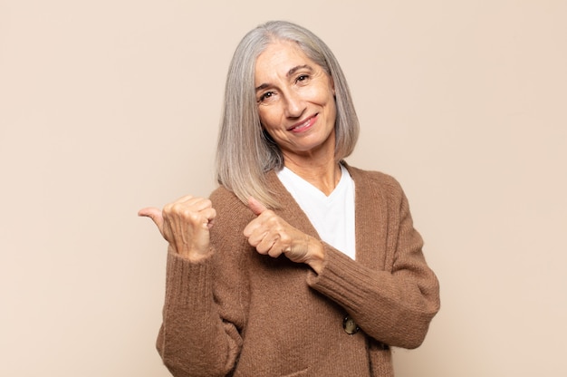 Mulher de meia-idade sorrindo alegre e casualmente apontando para uma cópia do espaço ao lado, sentindo-se feliz e satisfeita