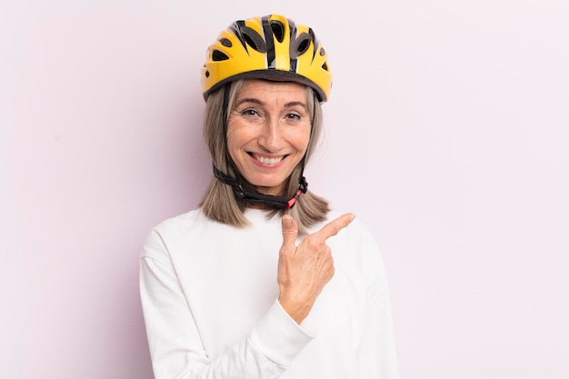 Mulher de meia idade sorrindo alegremente se sentindo feliz e apontando para o conceito de capacete de bicicleta lateral