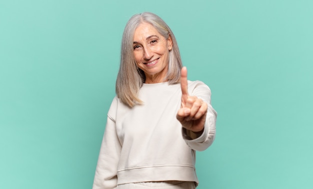 Foto mulher de meia-idade sorrindo com orgulho e confiança fazendo a pose número um triunfantemente, sentindo-se uma líder