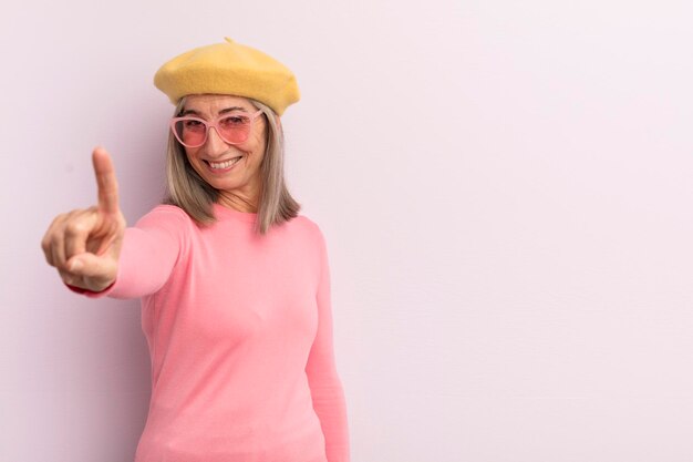 Mulher de meia idade sorrindo com orgulho e confiança fazendo o número um