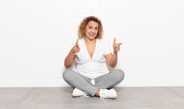 Mulher de meia-idade sorrindo com uma atitude positiva, bem-sucedida e feliz apontando para a câmera, fazendo sinal de arma com as mãos