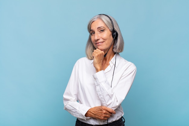 Mulher de meia idade sorrindo com uma expressão feliz e confiante com a mão no queixo, pensando e olhando para o lado. conceito de telemarketing