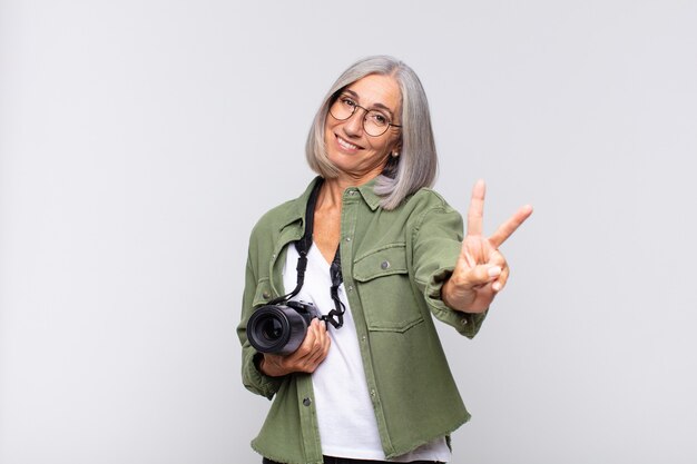 Mulher de meia idade sorrindo e parecendo amigável, mostrando o número dois ou o segundo com a mão para a frente, em contagem regressiva. conceito de fotógrafo