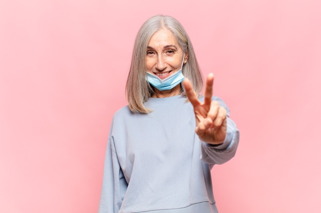 Mulher de meia-idade sorrindo e parecendo amigável, mostrando o número dois ou o segundo com a mão para a frente, em contagem regressiva