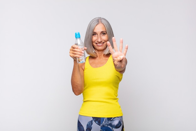 Mulher de meia-idade sorrindo e parecendo amigável, mostrando o número quatro ou o quarto com a mão para a frente, em contagem regressiva. conceito de fitness