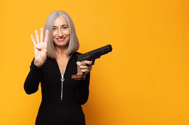 Mulher de meia idade sorrindo e parecendo amigável, mostrando o número quatro ou o quarto com a mão para a frente, em contagem regressiva