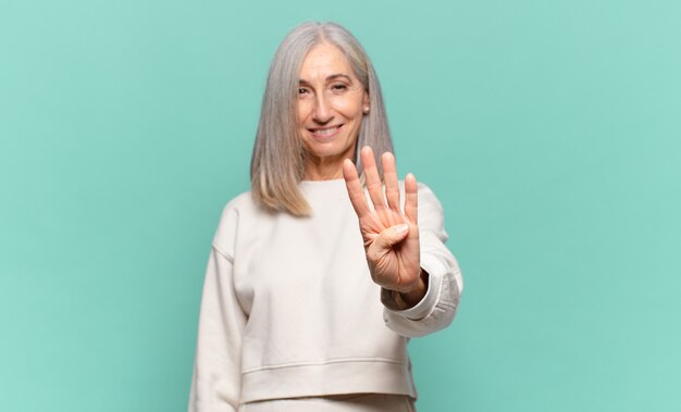 Mulher de meia-idade sorrindo e parecendo amigável, mostrando o número quatro ou o quarto com a mão para a frente, em contagem regressiva