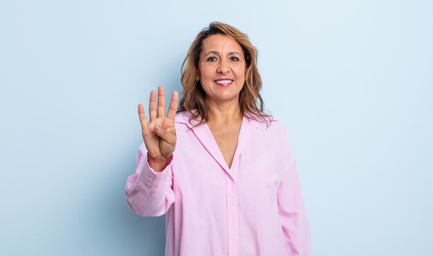 Mulher de meia idade sorrindo e parecendo amigável, mostrando o número quatro ou o quarto com a mão para a frente, em contagem regressiva