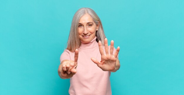 Mulher de meia idade sorrindo e parecendo amigável, mostrando o número seis ou sexto com a mão para a frente, em contagem regressiva