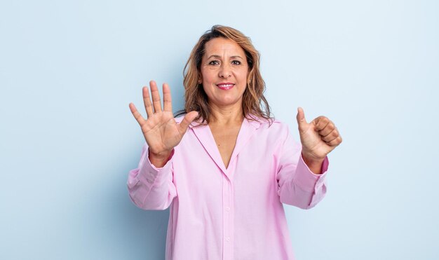 Mulher de meia-idade sorrindo e parecendo amigável, mostrando o número seis ou sexto com a mão para a frente, em contagem regressiva