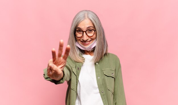 Mulher de meia idade sorrindo e parecendo amigável, mostrando o número três ou terceiro com a mão em contagem regressiva