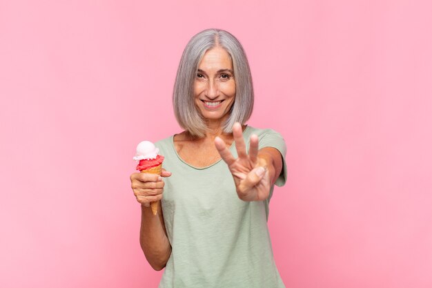 Mulher de meia idade sorrindo e parecendo amigável, mostrando o número três ou terceiro com a mão para a frente, em contagem regressiva tomando um sorvete