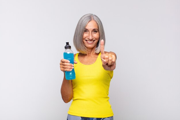 Mulher de meia-idade sorrindo e parecendo amigável, mostrando o número um ou primeiro com a mão para a frente, em contagem regressiva. conceito de fitness