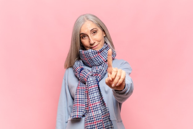 Mulher de meia idade sorrindo e parecendo amigável, mostrando o número um ou primeiro com a mão para a frente, em contagem regressiva